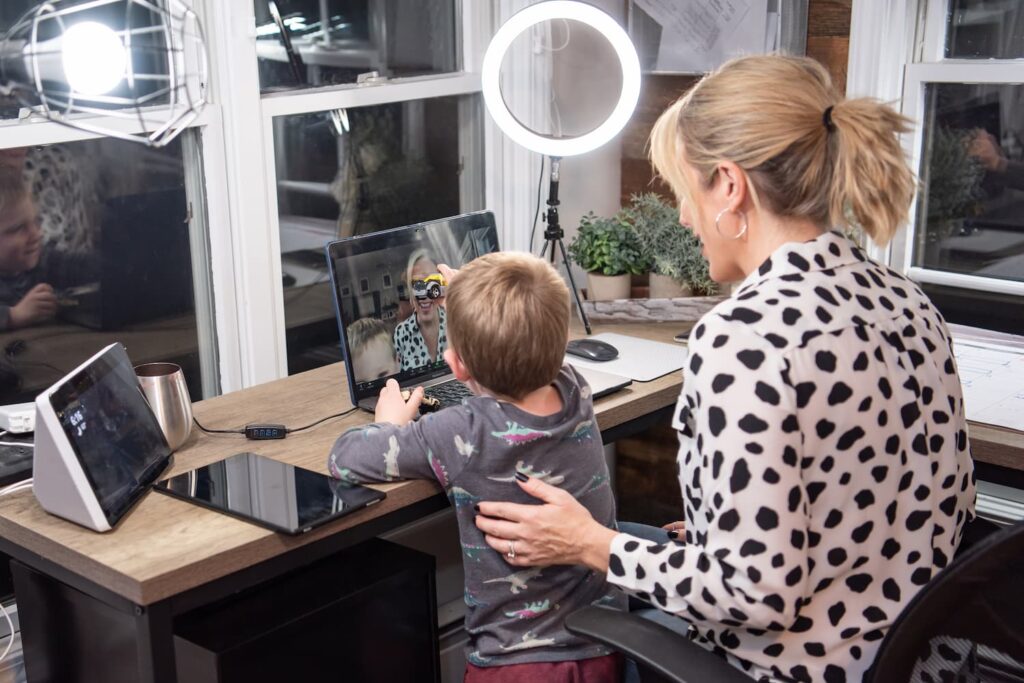 Kerry Barrett with her child Kerry Barrett and her child sitting at her desk in front of an opened laptop and an iPad.