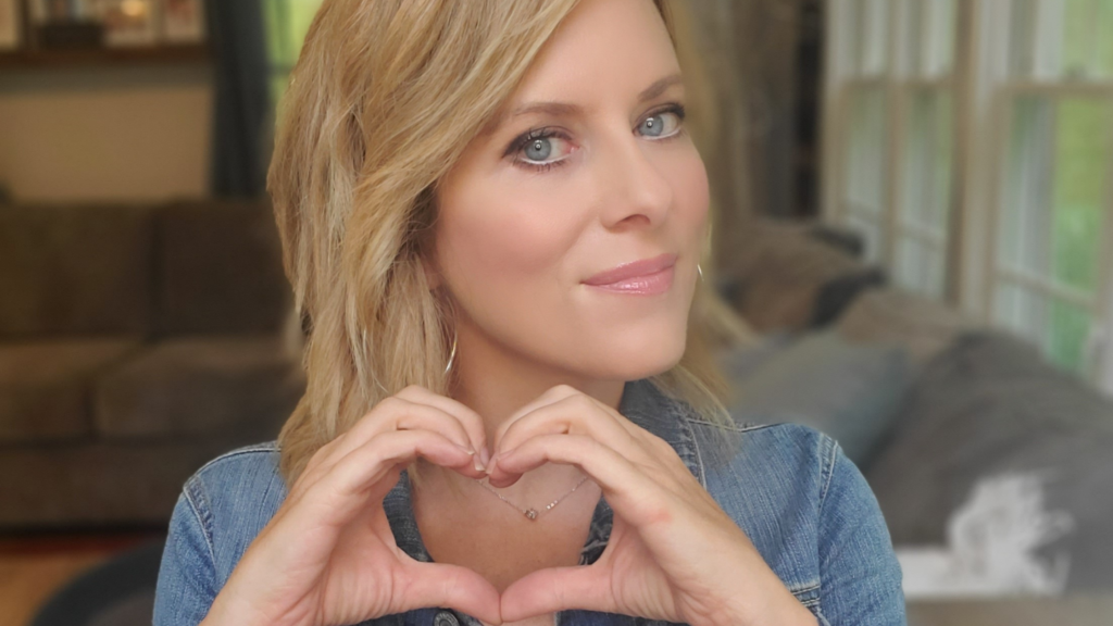 Kerry Barrett wearing a jean jacket and smiling subtly, while holding her hands together in a heart shape.