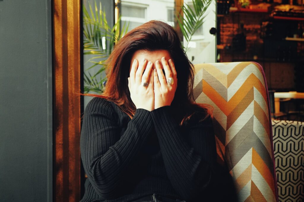 A person seated on a multicolor chair with their hands over their face.