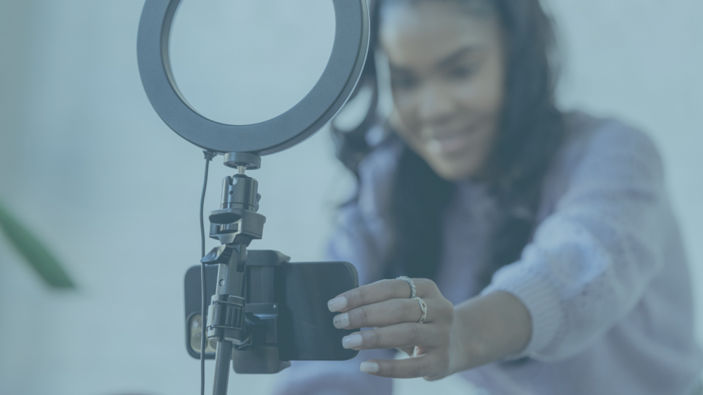 A young Black woman setting up a camera with a ring light, smiling slightly